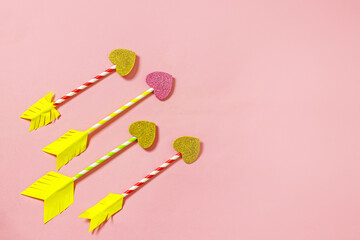 Valentine's day arrow heart background. Homemade arrows from cocktail straws and paper hearts on a pink background, top view, copy space. Creative love background