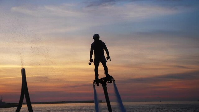 Silhouette of man with flyboard is making flip at sunset in slow motion. Amazing tricks with fly board. High quality 4k footage