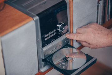 Senior man inserting a CD to the hi-fi station and listening the music