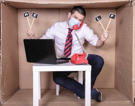 Businessman Works In An Uncomfortable Cardboard Office, Quietly Calls For Help, In The Meantime Talking On The Phone