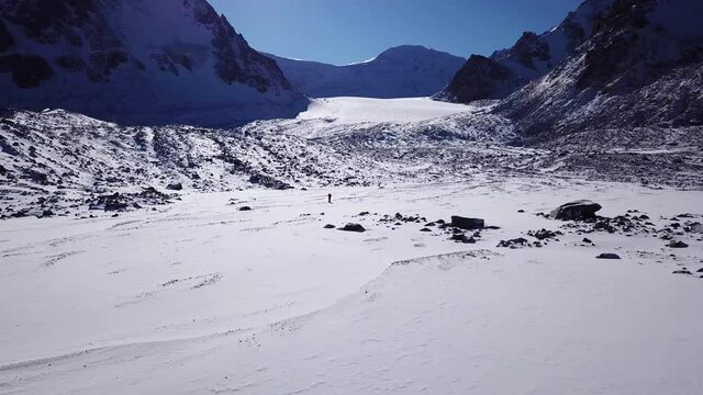 One climber is walking among the snowy mountains. Top view from a drone. The guy tramples the path. Tuyuk Su Glacier. high rocks and huge rocks. Clear blue sky. Sunny day. Extreme outdoor activities.
