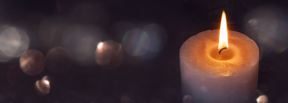 Candlelight in darkness with abstract blurred golden bokeh for religious ritual and funeral service or spiritual meditation. Background for peaceful mind and soul with space for text.