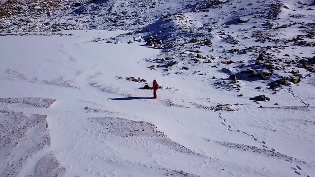 One climber is walking among the snowy mountains. Top view from a drone. The guy tramples the path. Tuyuk Su Glacier. high rocks and huge rocks. Clear blue sky. Sunny day. Extreme outdoor activities.