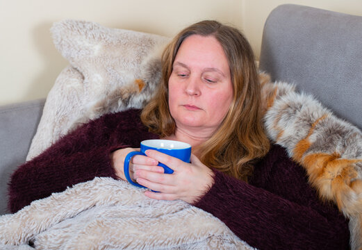 Frau liegt mit Covid-19 Symptome erkältet in einem Angora Pullover und Felldecke auf der Couch 