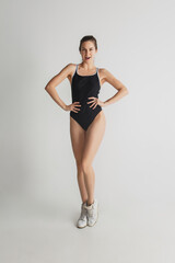 Fashion. Beautiful young woman's portrait isolated on grey studio background. Having fun, happy, full length. Dancing, getting crazy mood, having fun. Stylish girl in black sportive swimsuit