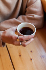 Young woman holds in hand ceramic white cup with black coffee or tea. alternative brewing of specialty coffee. light beige wood table background