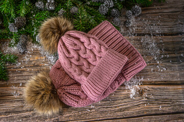 Warm knitted pink hats with pompom for mother and daughter. Christmas decoration on wooden background.