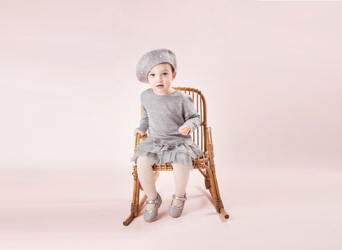 Ni&ntilde;a sentada en sillita con vestido gris y gorro