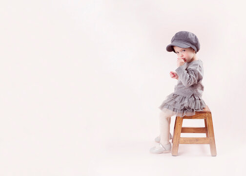 Ni&ntilde;a sentada en sillita con vestido gris y gorro