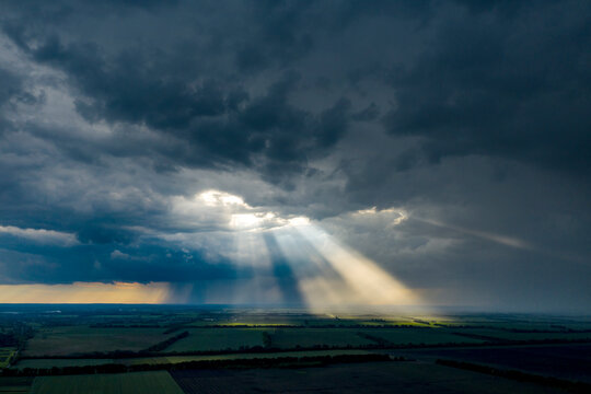 Aerial flying above stunning field under dramatic rain cloud rolling. Global warming effect black thunderstorm dramatic rain clouds Dramatic sky. Light rays shining through clouds - Powered by Adobe