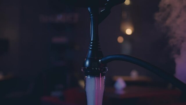 Close up of black hookah parts in the dark room, neon lights with smoke. Bar blurred background dark interior with hookah on the foreground 