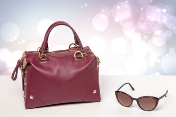 Luxury and stylish womens leather handbag and sunglasses on a bright glittering desk against abstract pastel background. Advertising elegant women accessories.