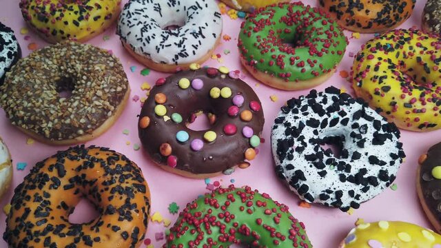 assorted donuts with icing a pink background. Background of assorted doughnuts with different flavors. The video dolly