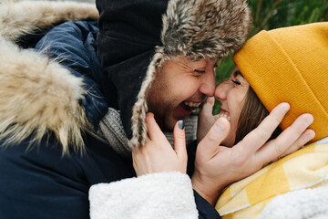 Happy couple in love holding each other's faces, touching noses and laughing. They both are dressed for winter.