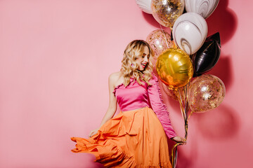 Fototapeta na wymiar Cute girl in orange skirt dancing at party. Romantic blonde female model celebrating birthday.