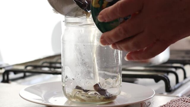 Female hand pours brine and marinate or fermented mushrooms into a glass jar. Armillaria mellea