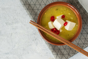  horizontal top view of japanese or asian spicy miso soup with tofu and red pepper in a brown bowl on a stand with chopsticks  with copy space