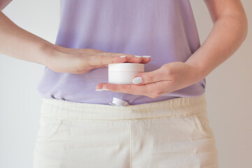 Young woman uses face and neckline care cream. Woman holds a jar of cream with natural ingredients to preserve youth and rejuvenate the skin of her hands, face and body.