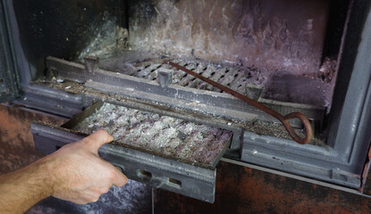 Fireplace cleaning. Man hand holds a shovel with ash.A hand collects ash from the fireplace on an old steel blade. Daily winter routine