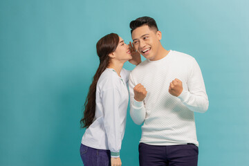 Tell me your secrets. Pleasant smiling asian woman whispering on ear to her man something important, blue background - obrazy, fototapety, plakaty