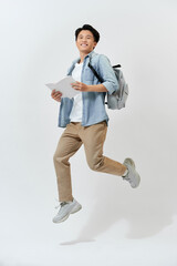Happy young Asian student man jumping in air with backpack and holding book over white background.