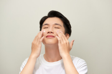 Portrait of satisfied young man applying facial cream isolated over white background