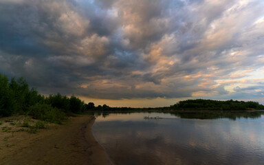 Summer landscape with the setting sun and clouds over the water.