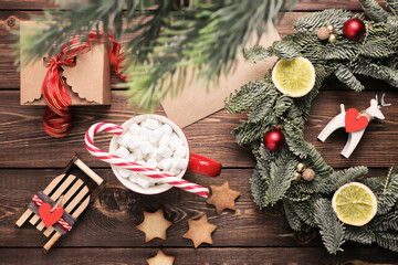 Christmas wreath, gift, coffee mug with marshmallows, envelope and homemade cookies and various Christmas decorations on the wooden table. Rustic christmas wreath, flat lay.