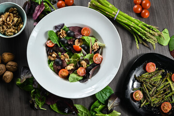 Delicious salad of cherry tomatoes, black olives, walnuts, assorted lettuce, sprouts, and fresh asparagus. Gourmet salad.