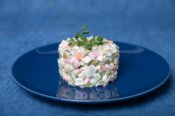 Olivier salad on a blue plate, decorated with pea sprouts. Traditional New Year and Christmas Russian salad. Close-up, selective focus, blue background.