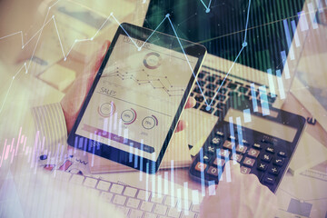 Double exposure of man's hands holding and using a digital device and forex graph drawing. Financial market concept.