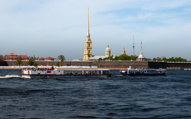 Pleasure and excursion boats run along the Neva River past the Peter and Paul Fortress 1703. Yellow spire and dark blue water. St. Petersburg, Russia.