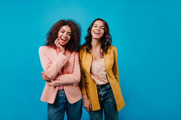 Confident girls standing on blue background. Amazing african woman posing next to her friend.