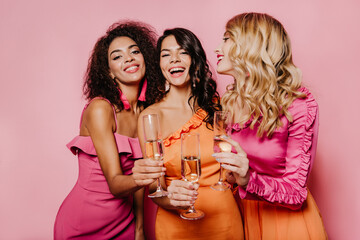 Fashionable girls raising glasses. Studio photo of laughing friends drinking champagne.