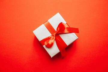 Gift box wrapped in craft paper with red ribbon bow on red background. Modern creative minimal solid color holiday composition