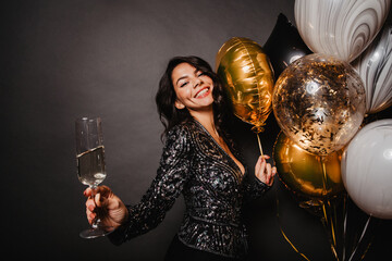Pleased latin girl standing near party balloons. Enchanting young woman drinking wine in her...