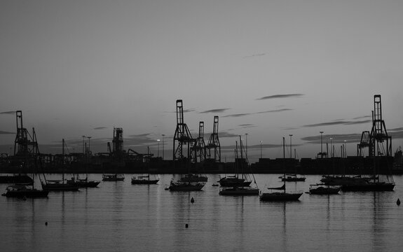 Backlit image of the harbor at dawn with many sailboats and large cranes, Las Palmas of Gran Canaria
