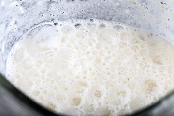 Blender cup with soy milk, top view. Freshly prepared plant milk drink with bubbles on surface.