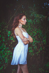 A beautiful woman stands among the green thickets of trees. The concept of beauty and ecology.