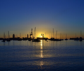 Fototapeta premium Sunrise in the bay with calm sea, intense blue sky and backlit port with many ships