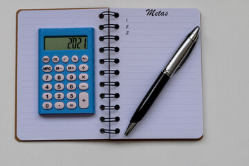 goals for 2021, calculator, pen and notepad. Translation: goals, in Portuguese.