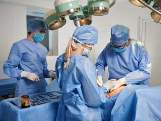 Group of doctors doing cosmetic surgery in operating room. Surgical team wearing protective face masks, sterile gloves and medical caps while performing aesthetic surgery in clinic.