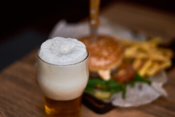 A glass of beer with foam and a burger