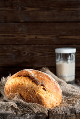 Loaf of homemade white milk sourdough bread, selective focus. A glass of sourdough on the table. Close-up, with copy space. Craft bread on a fabric lining, wooden background