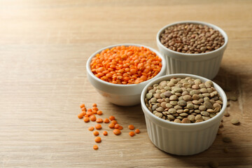 Bowls with different legumes on wooden background, space for text