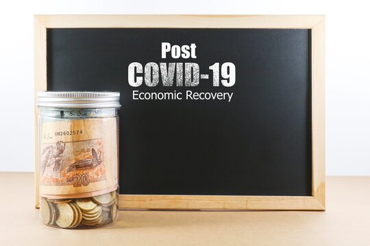 Business And People Concept.  Coins And Banknotes In A Jar With A Message On Post Covid19 Economic Recovery On The Black Chalkboard