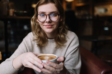 Woman in eyeglasses drinking cup of hot drink in cafe
