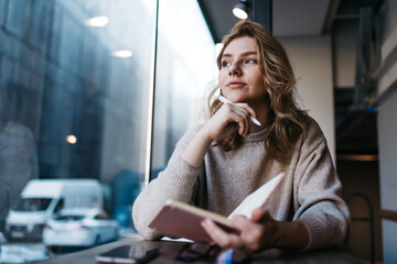 Thoughtful young woman creating article in cafe