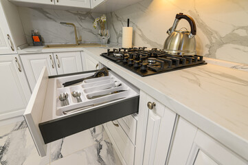 Open drawers with kitchenware at modern white kitchen