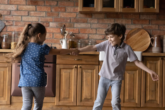 Carefree Children. Happy Joyful Small Kids Siblings Brother Sister Spinning Around Kitchen Holding Hands. Diverse Junior Friends Boy Girl Play Active Game Dancing Running Having Fun Enjoying Holiday